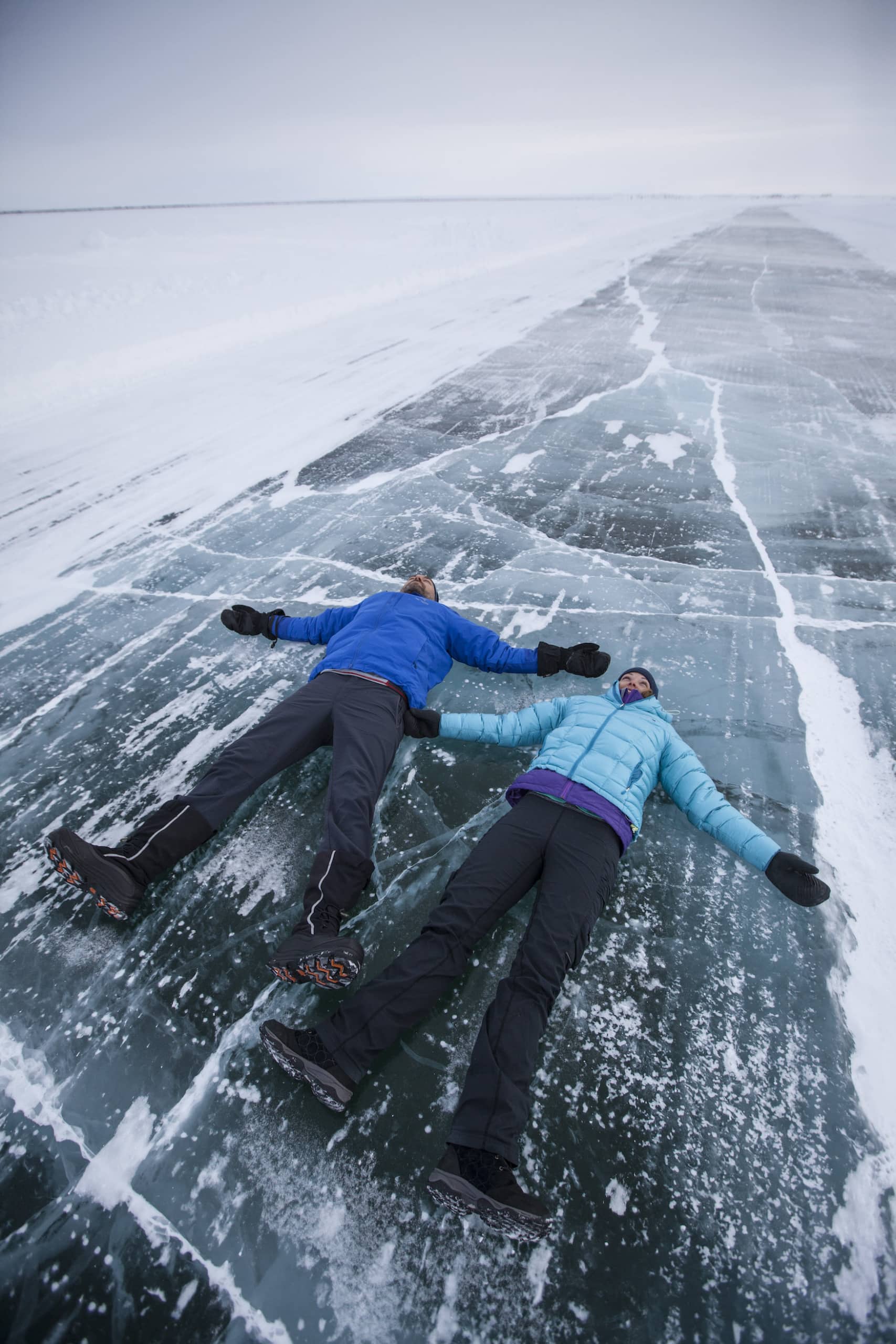 Zwei Menschen liegen in Winterjacken auf zugefrorener Straße