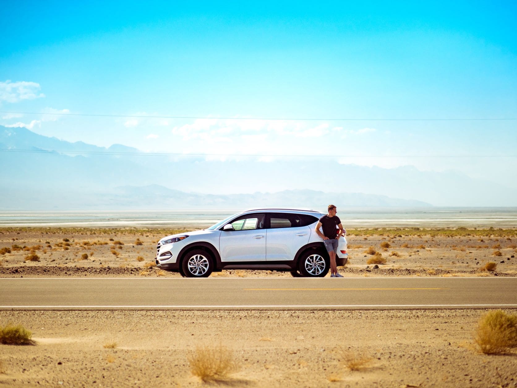 Mann lehnt an SUV in der Wüste 