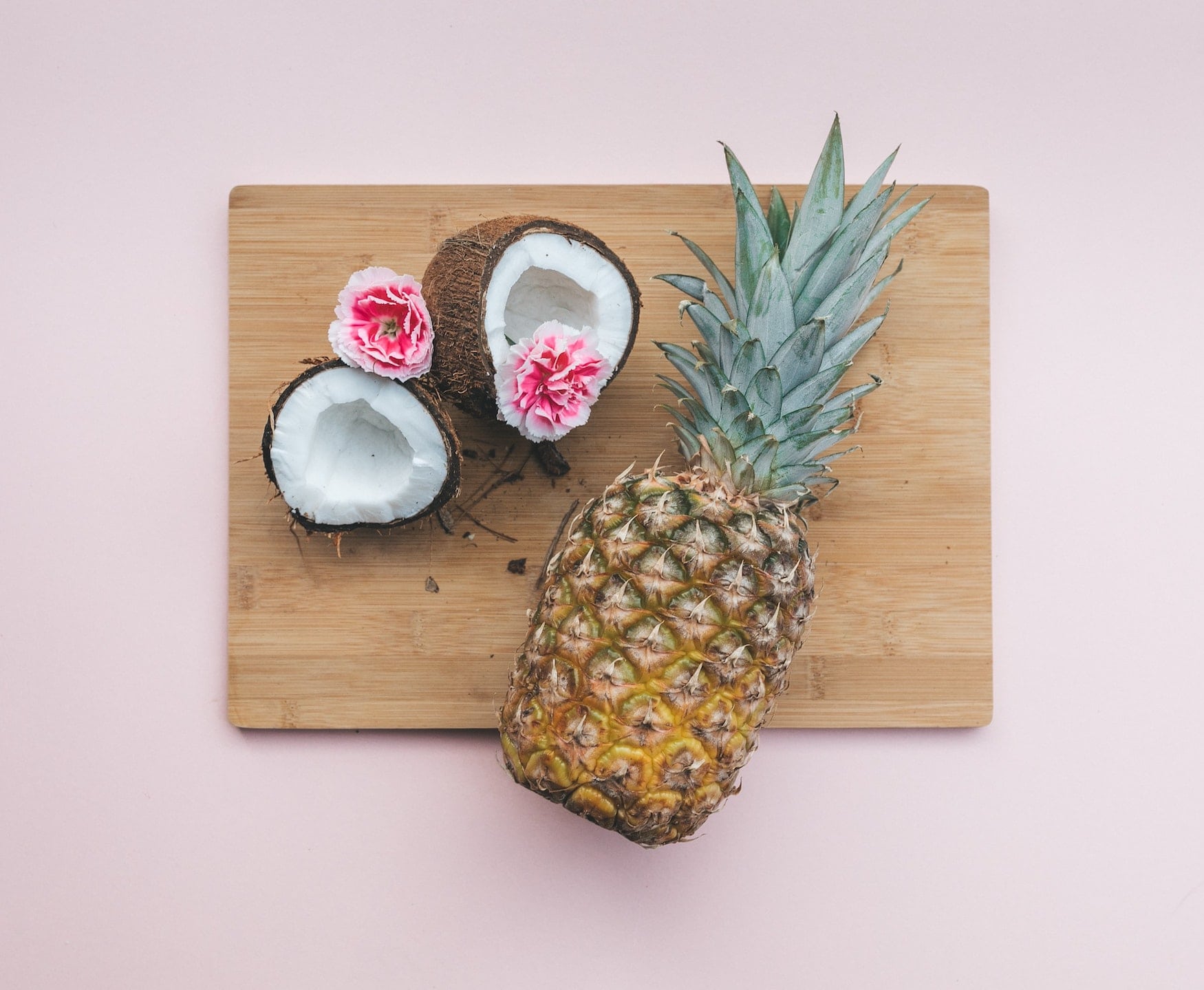 Frische Ananas und Kokosnüsse auf einem Holzbrett serviert vor pinkem Hintergrund