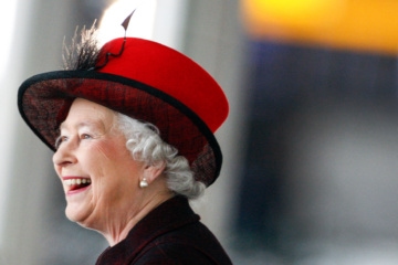 Queen Elizabeth II. lächelt und trägt einen roten Hut