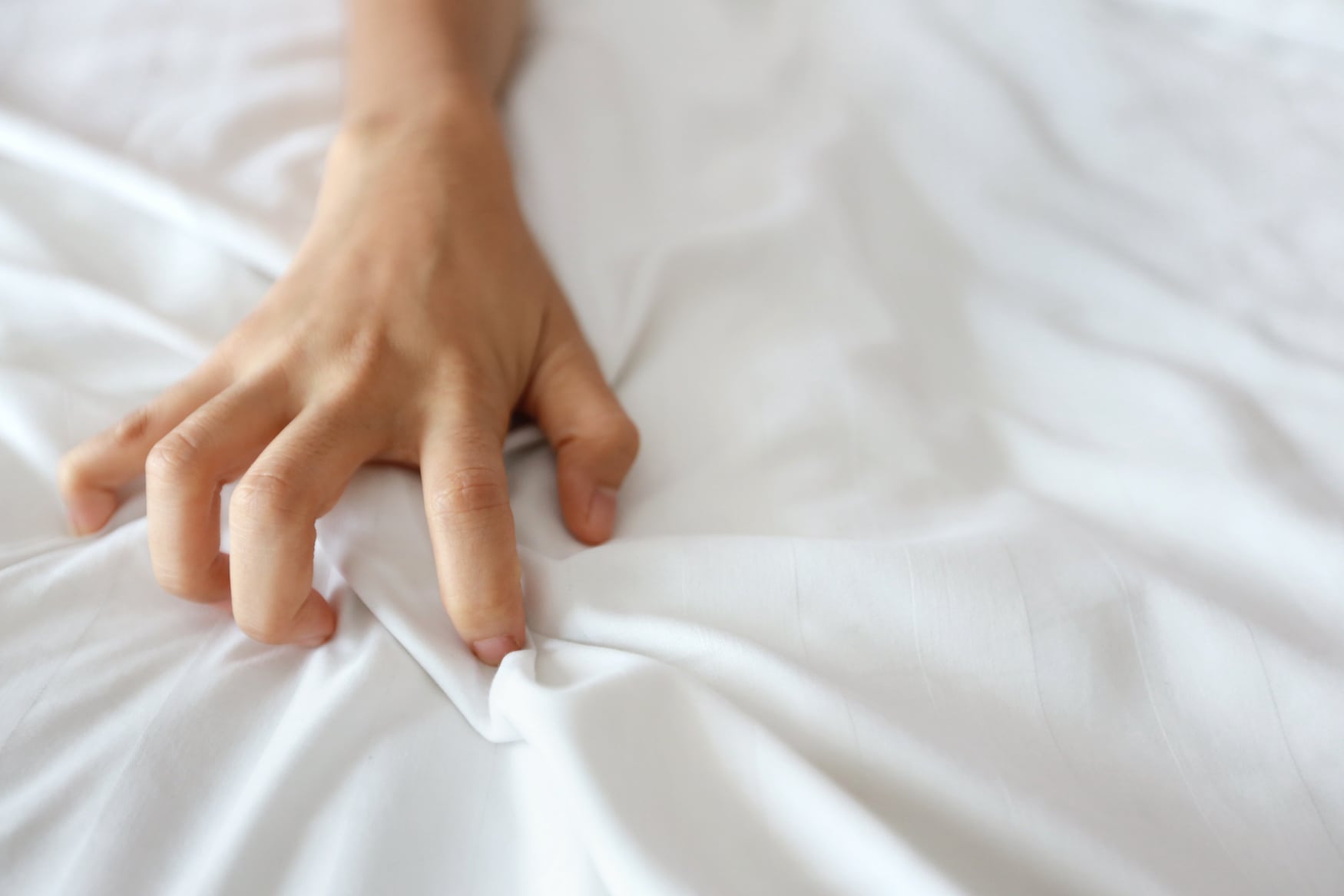 Hand greift Bettlaken während Sex im Hotel