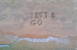 An einem Strand sind die Wörter "Test & Go" in den Sand gemalt