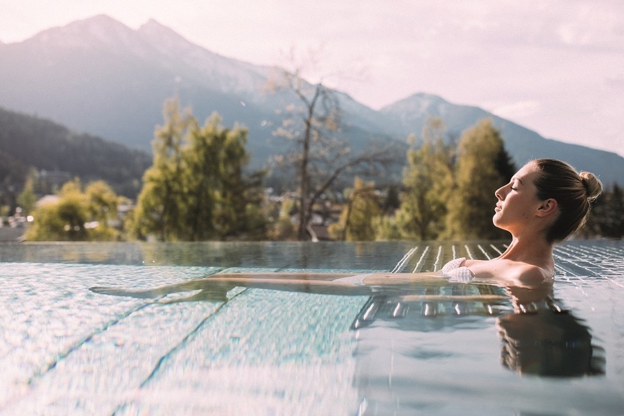 Frau entspannt in Infinity-Pool vor der Tiroler Bergwelt