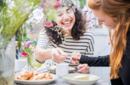 Zwei junge Frauen begehen gemeinsam die schwedische "Fika", eine traditionelle Kaffeepause, an einem frühlingshaft gedeckten Tisch.