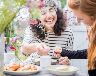 Zwei junge Frauen begehen gemeinsam die schwedische "Fika", eine traditionelle Kaffeepause, an einem frühlingshaft gedeckten Tisch.