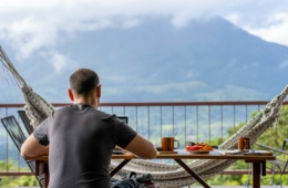 Mann sitzt auf Balkon in Costa Rica, frühstückt und arbeitet am Notebook