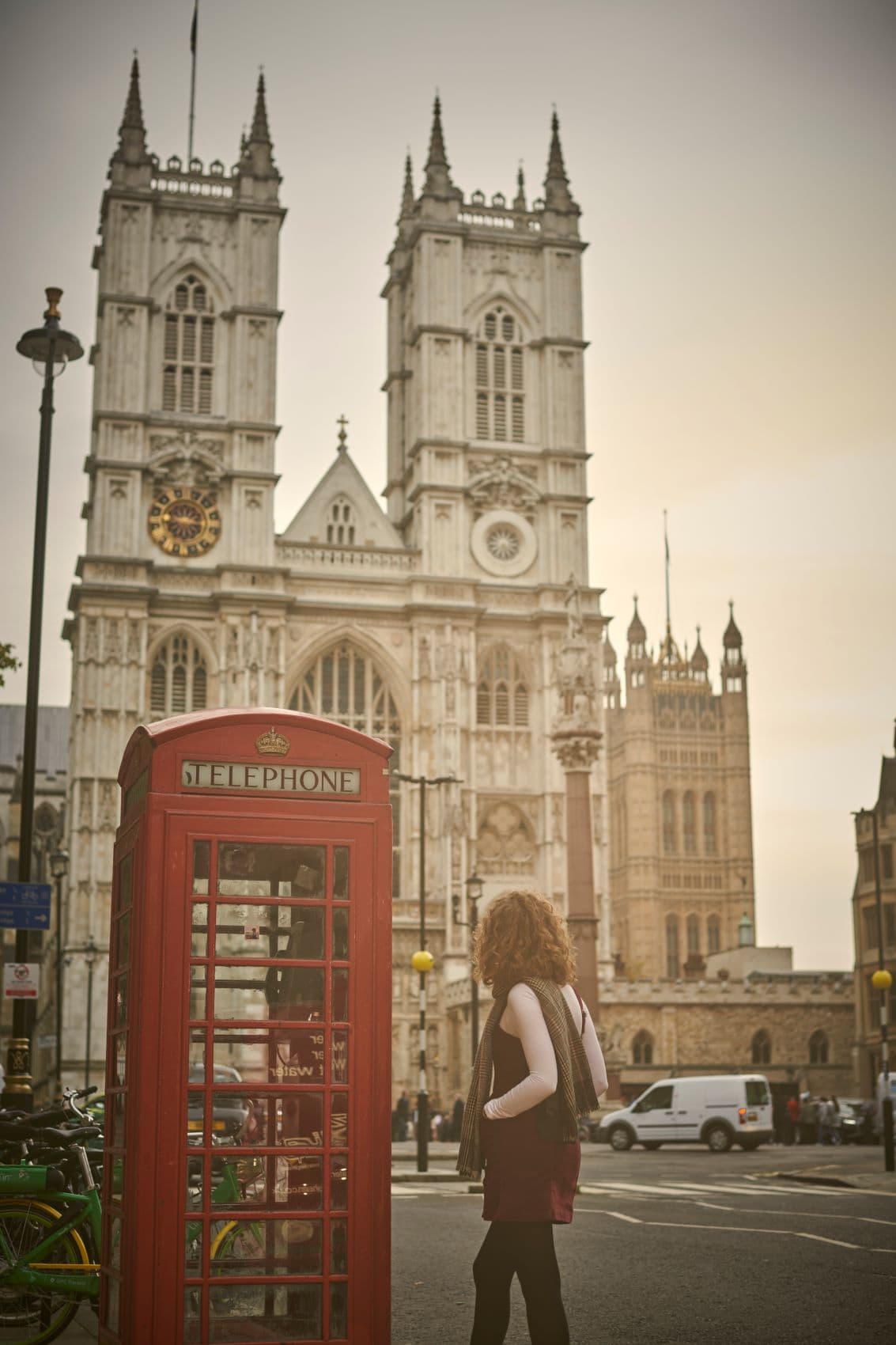 Frau neben Telefonzelle blickt auf Westminster Abbey 