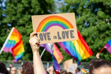 Frau hält auf Pride-Festival Schild mit "Love is Love"-Aufschrift