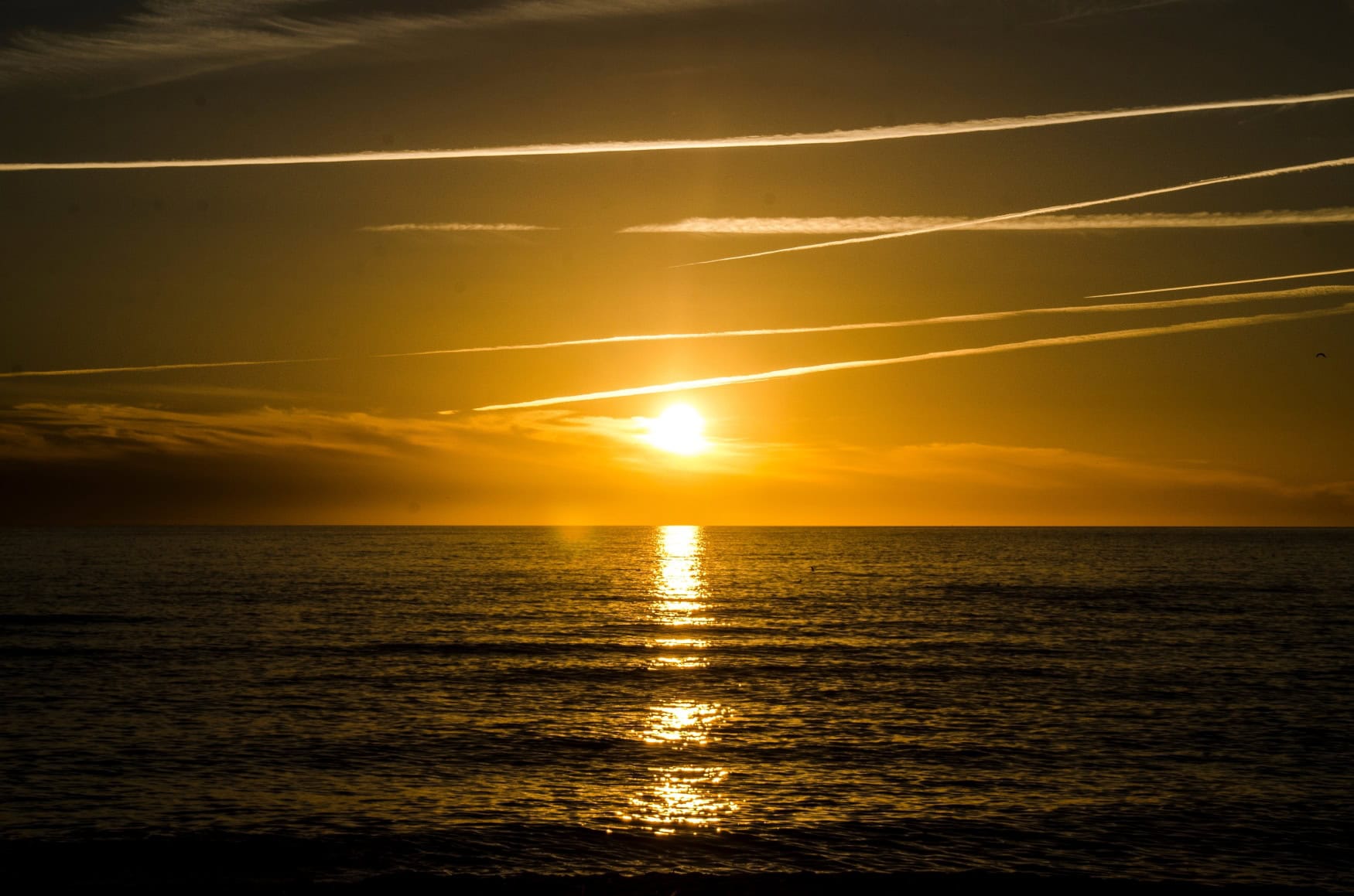 Über der in leichten Wellen liegenden Nordsee vor Sylt geht die Sonne goldgelb unter.