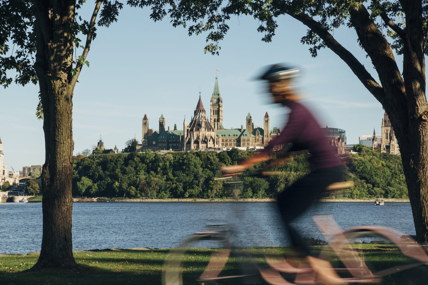Fahrradfahrerin fährt entlang des Ottawa Rivers, im Hintergrund das Parlament