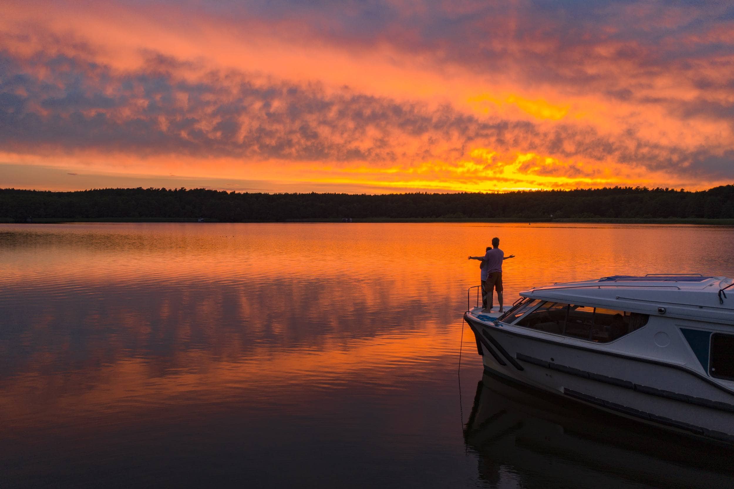 Pärchen steht auf dem Bug eines Hausbootes bei malerischen Sonnenuntergang am See