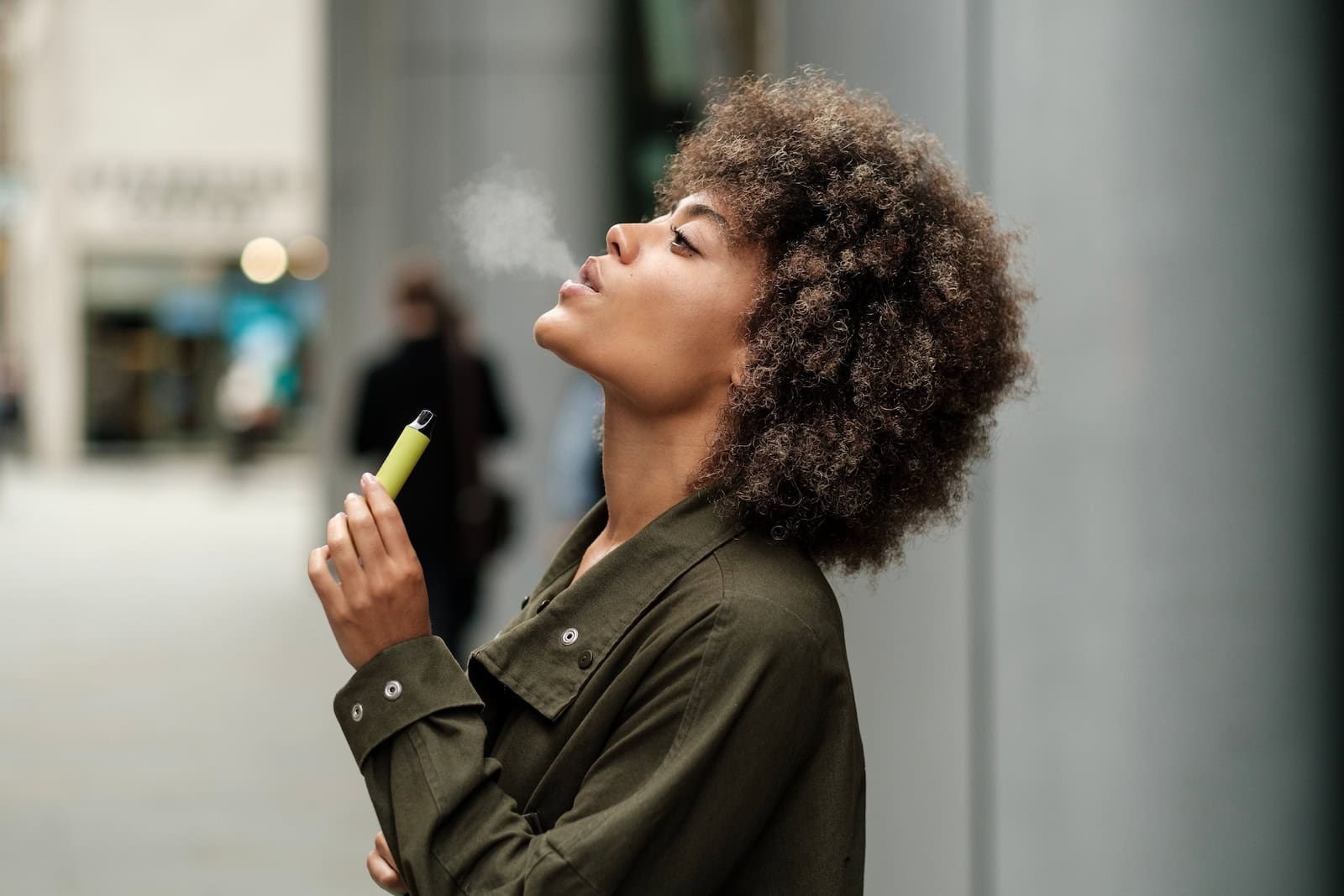 Frau raucht Vape vor einem Flughafen. Darf sie den Vape auch zollfrei mitnehmen?