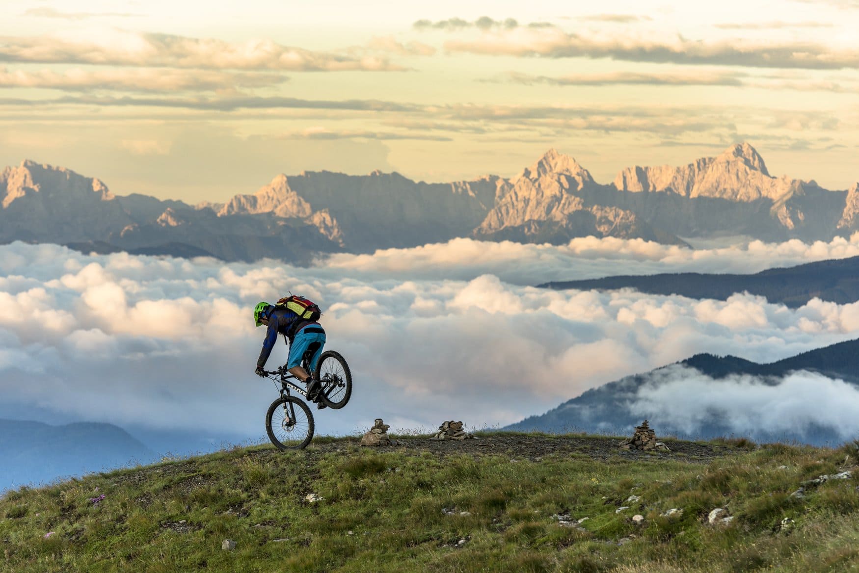 Ein Mountainbiker fährt über eine Bergkuppe am Flow Country Trail bei Bad Kleinkirchheim. Hinter ihm reicht eine geschlossene Wolkendecke bis zu den Gipfeln der Julischen Alpen.