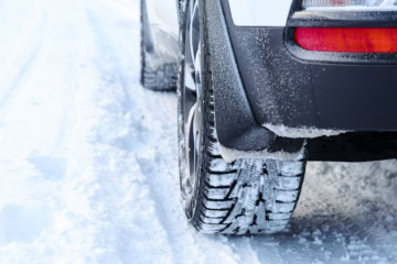 Nahaufnahme Winterreifen an Auto auf verschneiter Straße