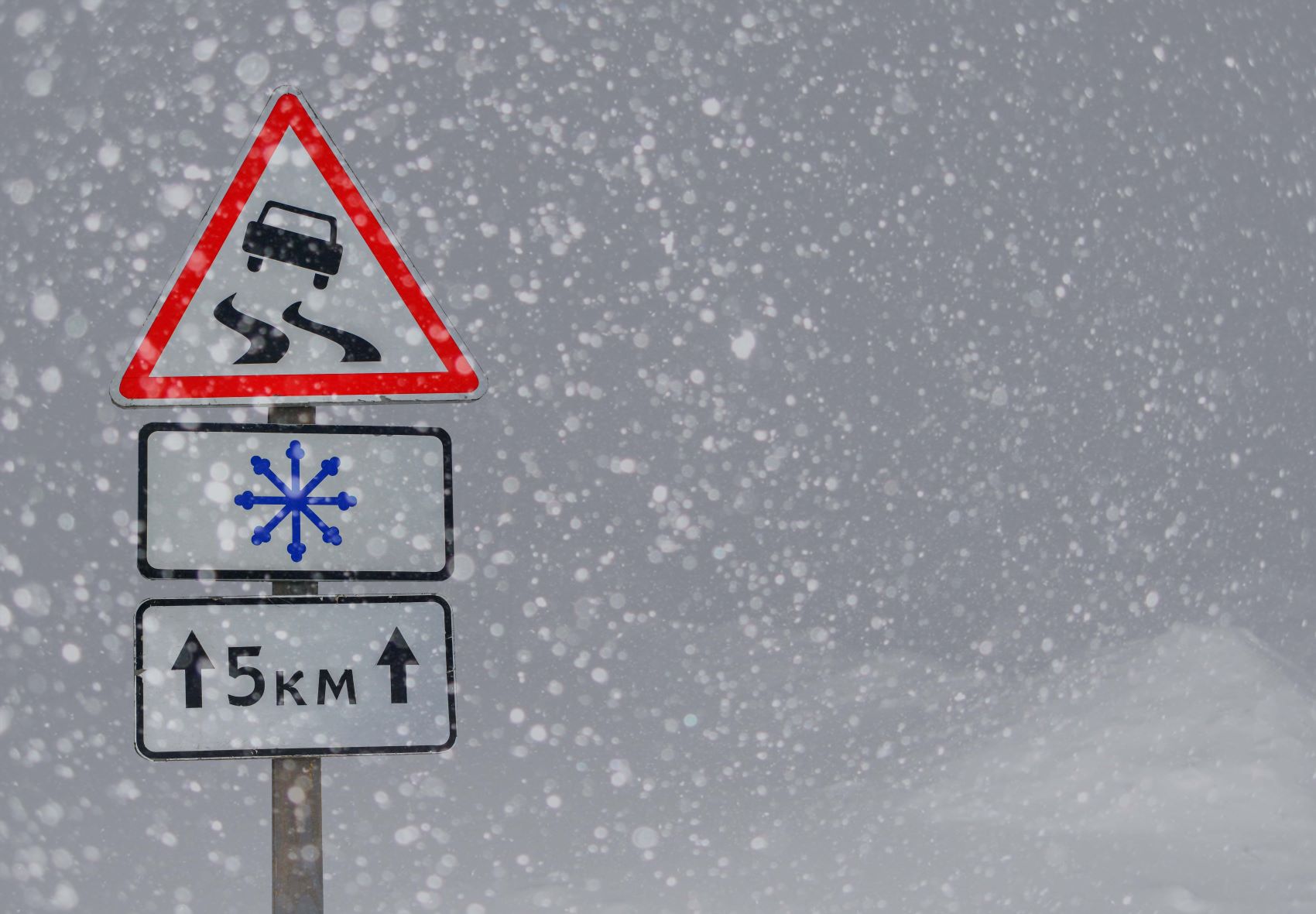 Verkehrsschild, das vor Glätte bei Schneefall warnt 