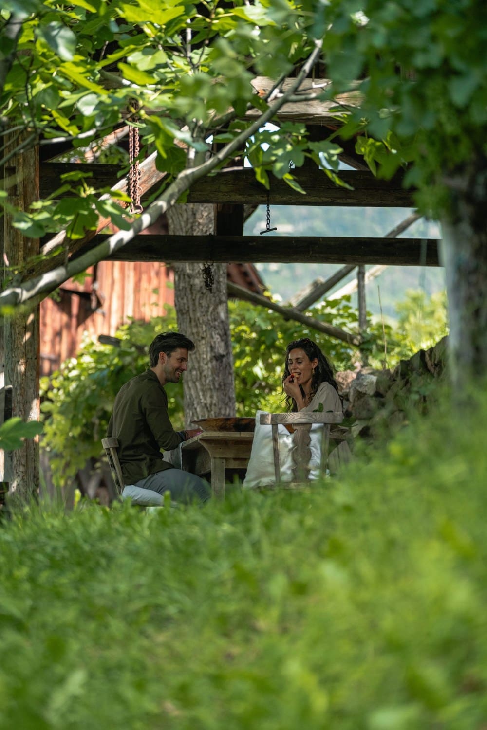 Ein Paar sitzt unter einer alten Holzpergola im Garten des Weinguts Grottnerhof in Völs am Schlern.