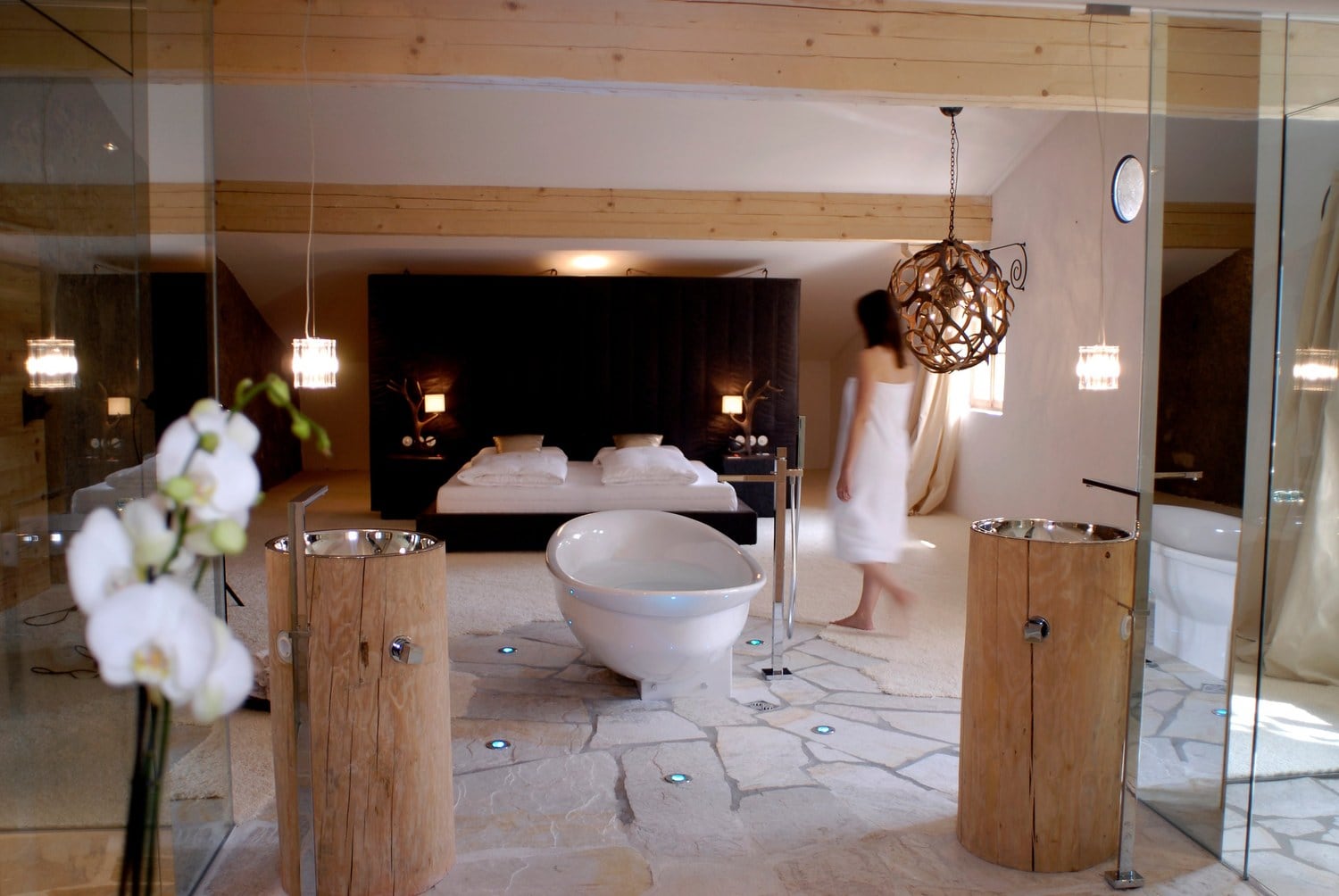 Suite mit freistehender Badewanne, Waschbecken auf Holzstämmen und Natursteinboden am Weingut Grottnerhof in Völs am Schlern.