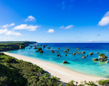 An einem tropischen Strand in Okinawa, Japan, ragen mehrere kleine Felsen aus dem Meer in einer Bucht.
