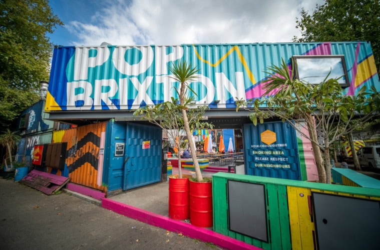 Mehrere bunt bemalte Schiffscontainer sind zu einer Art Tor aufgestapelt. Auf dem obersten ist in großer Schrift "Pop Brixton" zu lesen.