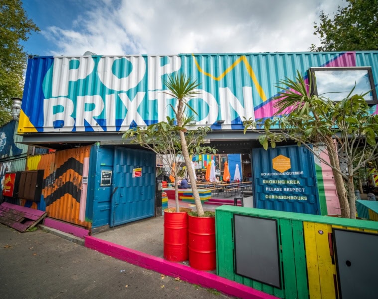 Mehrere bunt bemalte Schiffscontainer sind zu einer Art Tor aufgestapelt. Auf dem obersten ist in großer Schrift "Pop Brixton" zu lesen.