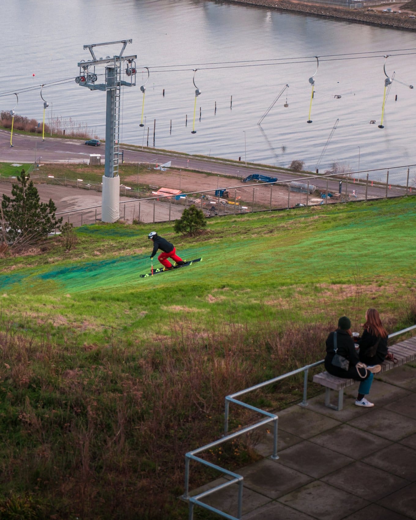 Skifahrer fährt grüne Piste in CopenHill runter, beobachtet von zwei Damen auf einer Parkbank.