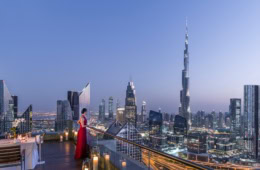 Eine Frau in rotem Abendkleid blickt von der Dachterrasse des Shangri-La Dubai auf die Dämmerung über der Skyline von Dubai