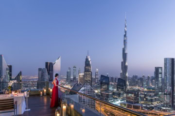 Eine Frau in rotem Abendkleid blickt von der Dachterrasse des Shangri-La Dubai auf die Dämmerung über der Skyline von Dubai