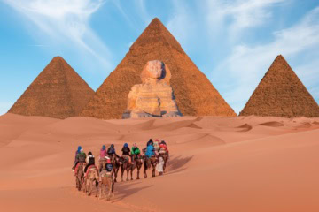 Touristen reiten auf Kamelen auf die Pyramiden von Gizeh zu.