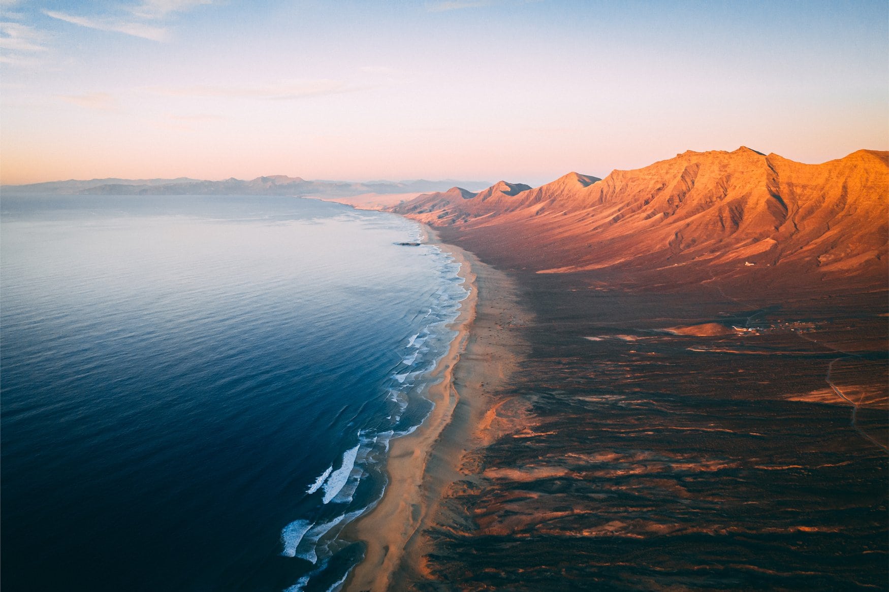 Luftaufnahme der Playa de Cofete auf Fuerteventura im Abendlicht: ein kilometerlanger Sandstrand zieht sich am Fuß des Bergrückens entlang der Atlantikküste.