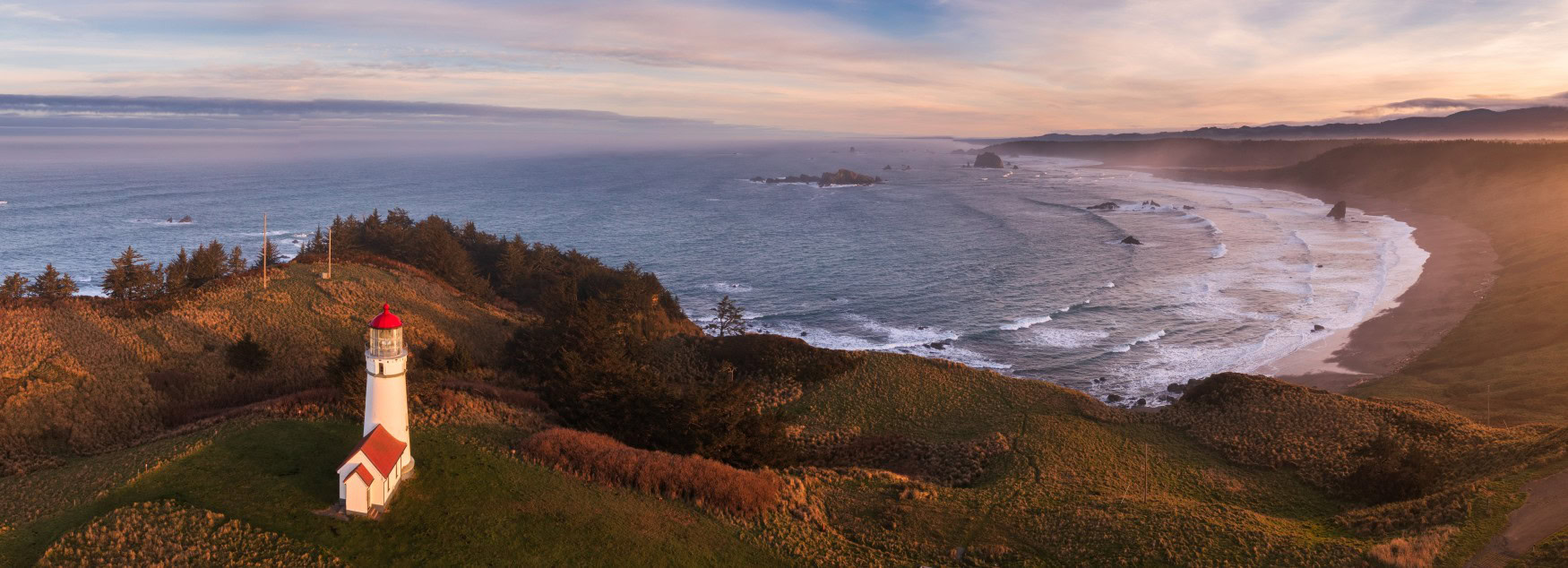 Luftaufnahme es Leuchtturms am Cape Blanco in Oregon; der weiße Leuchtturm steht einsam auf einer Landzunge, rechts davon liegt eine Pazifikbucht.