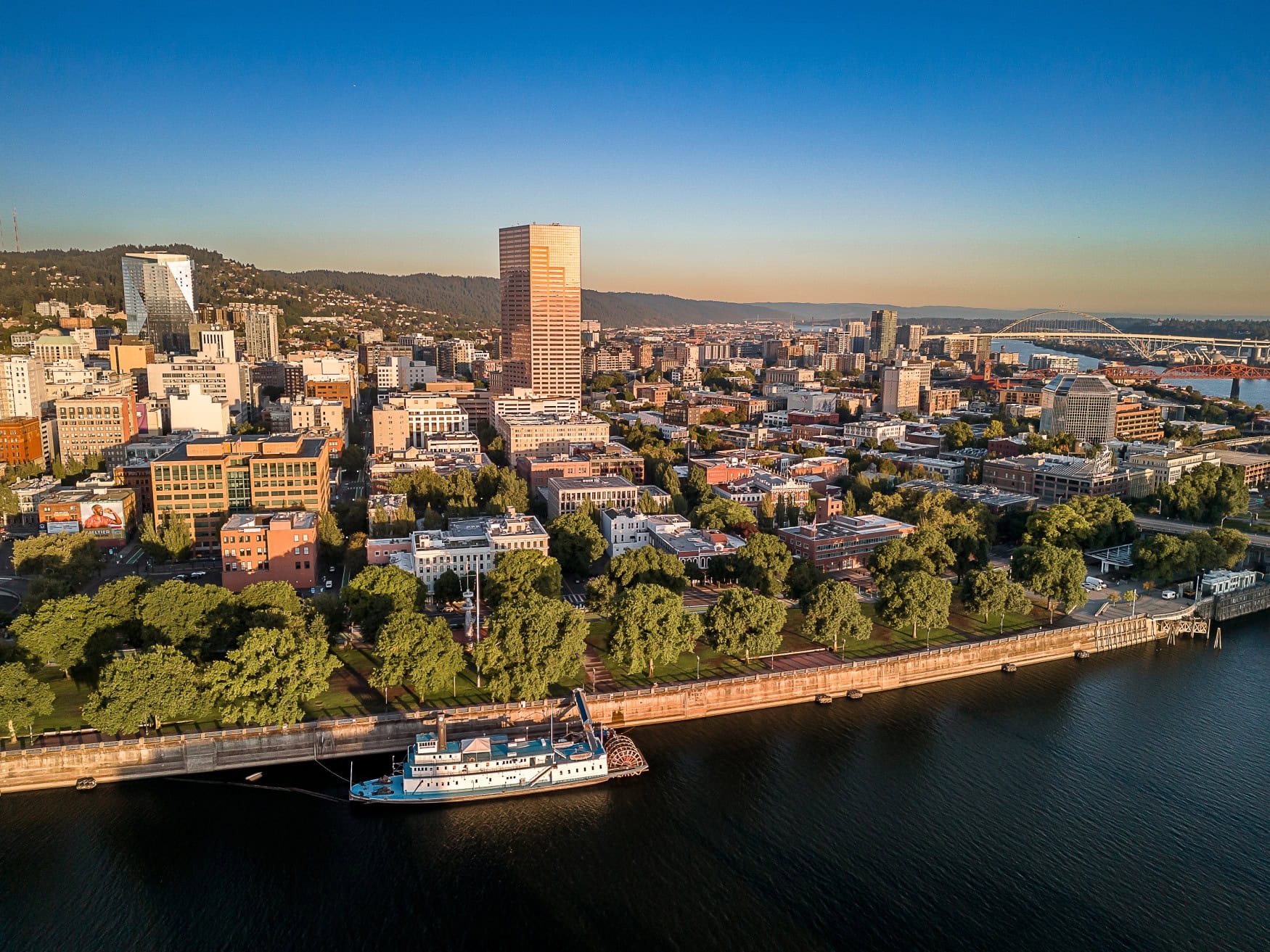 Die Innenstadt von Portland, Oregon, liegt im Licht der aufgehenden Sonne; Drohnenaufnahme mit dem Fluss im Vordergrund.