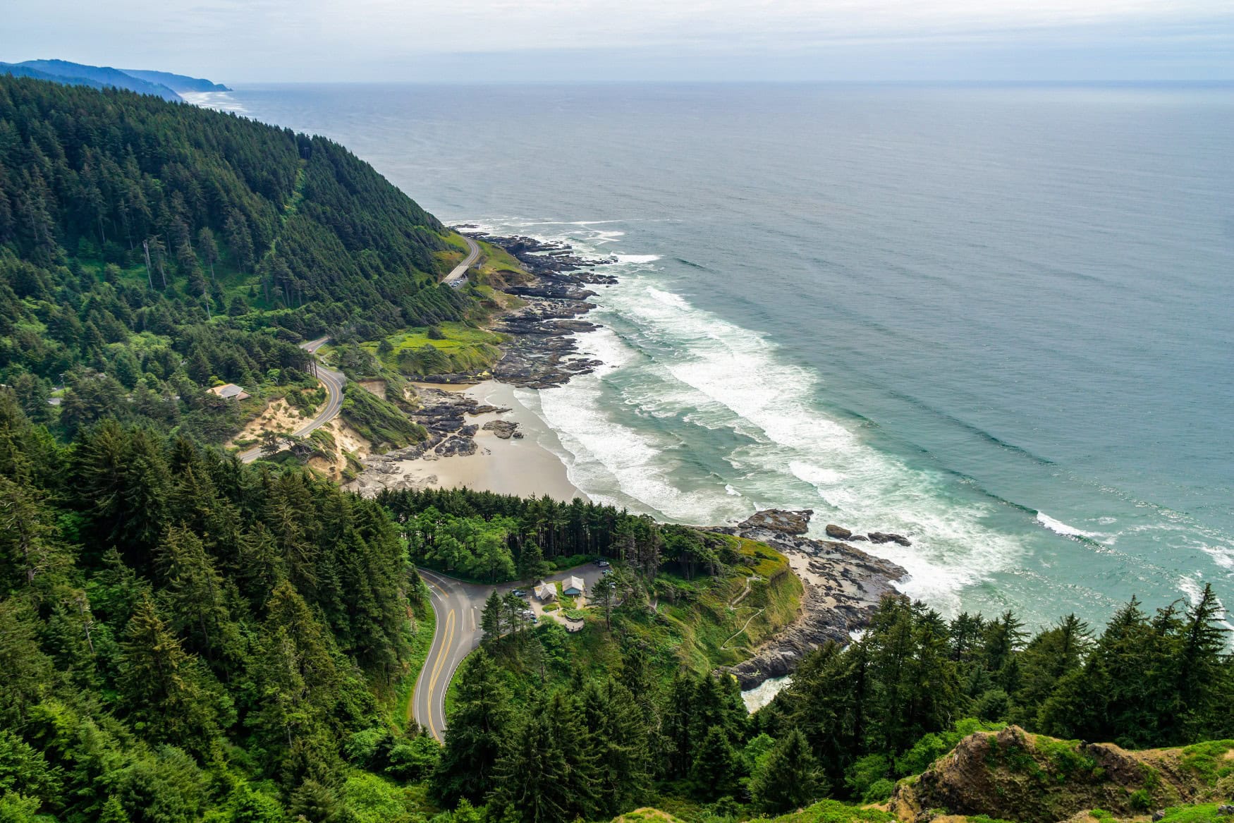 Luftaufnahme es Pacific Coast Scenic Byway in Oregon; links dichter Wald, durch den die Straße führt, rechts der Pazifik.