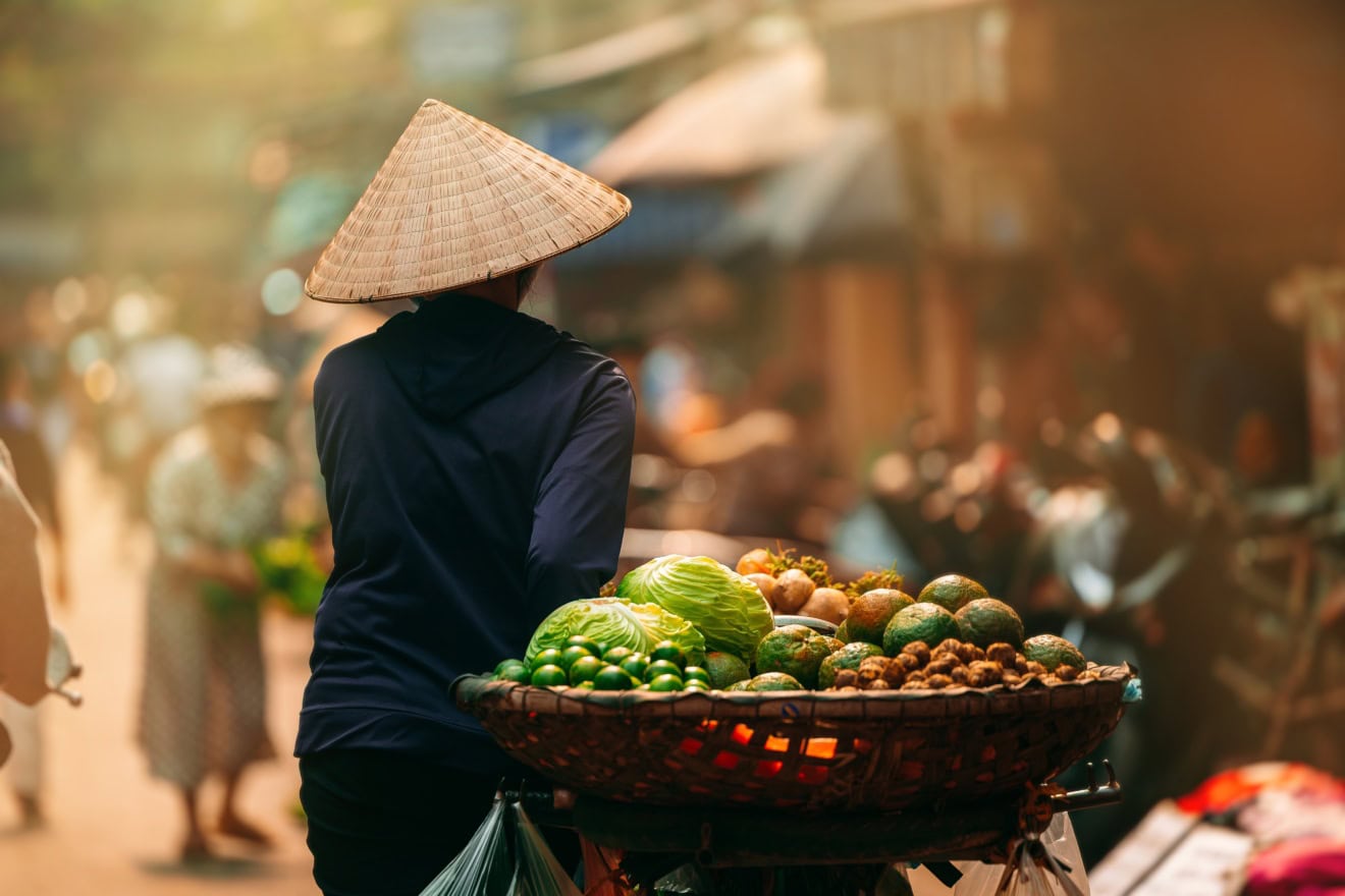 Eine Frau führt in Vietnam mit einem beladenen Fahrrad durch eine Straße.