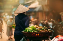 Eine Frau führt in Vietnam mit einem beladenen Fahrrad durch eine Straße.