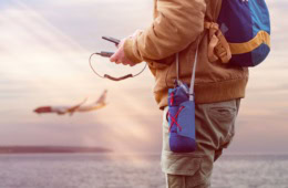 Reisender hält Powerbank und Handy in seiner Hand, im Hintergrund ein Flugzeug