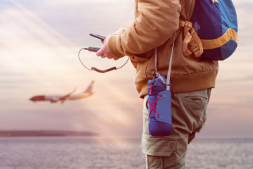 Reisender hält Powerbank und Handy in seiner Hand, im Hintergrund ein Flugzeug