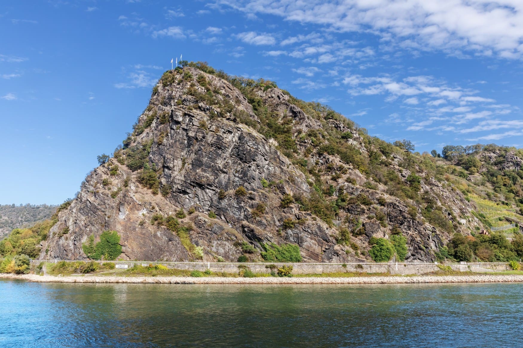 Der Loreley-Felsen am Mittelrhein in der Sommersonne, vom gegenüberliegenden Ufer aus gesehen.