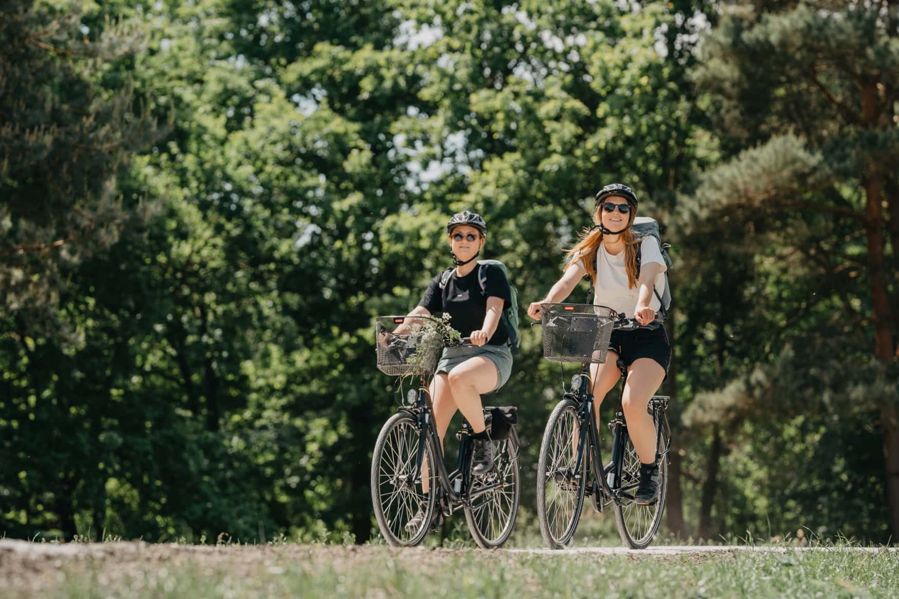 Zwei Frauen in sommerlicher Sportkleidung fahren über eine Wiese, im Hintergrund Wald.