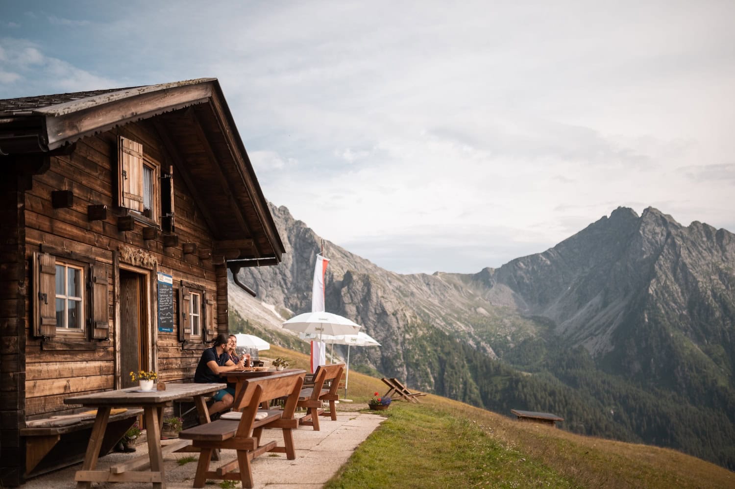 zwei Menschen auf einer Almhütte mit Aussicht auf die Berge