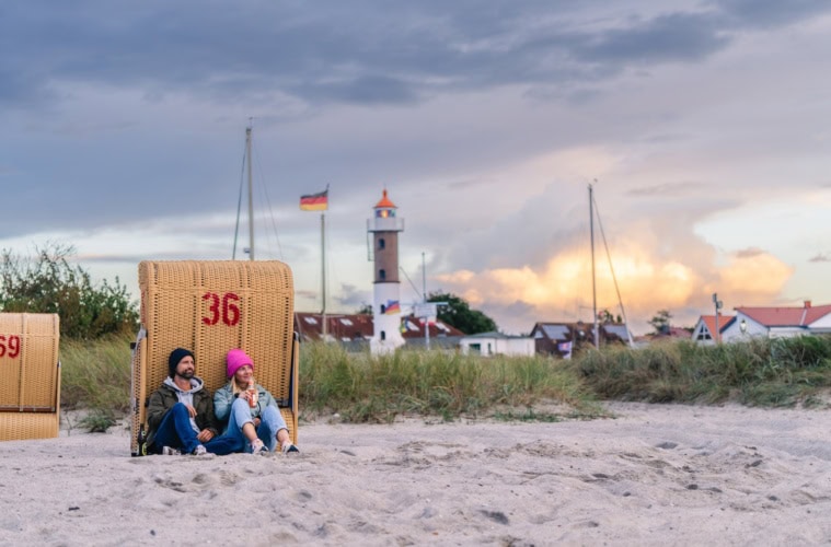 Ein Paar sitzt vor einem Strandkorb mit einer Flasche Bier beim Sonnenuntergang am Timmendorf Strand von Poel