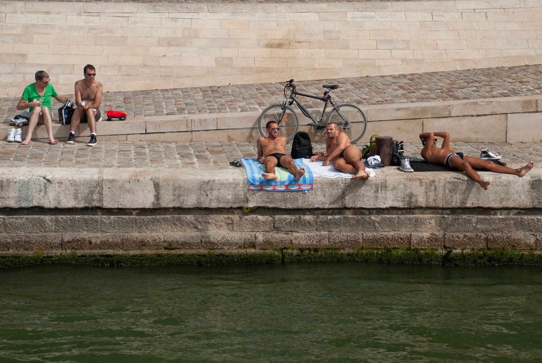 Männer in Badehosen sitzen an der Seine in Paris.