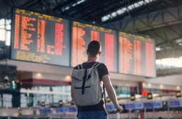 Junger Reisender am Flughafen blickt auf große Flug-Anzeigetafel