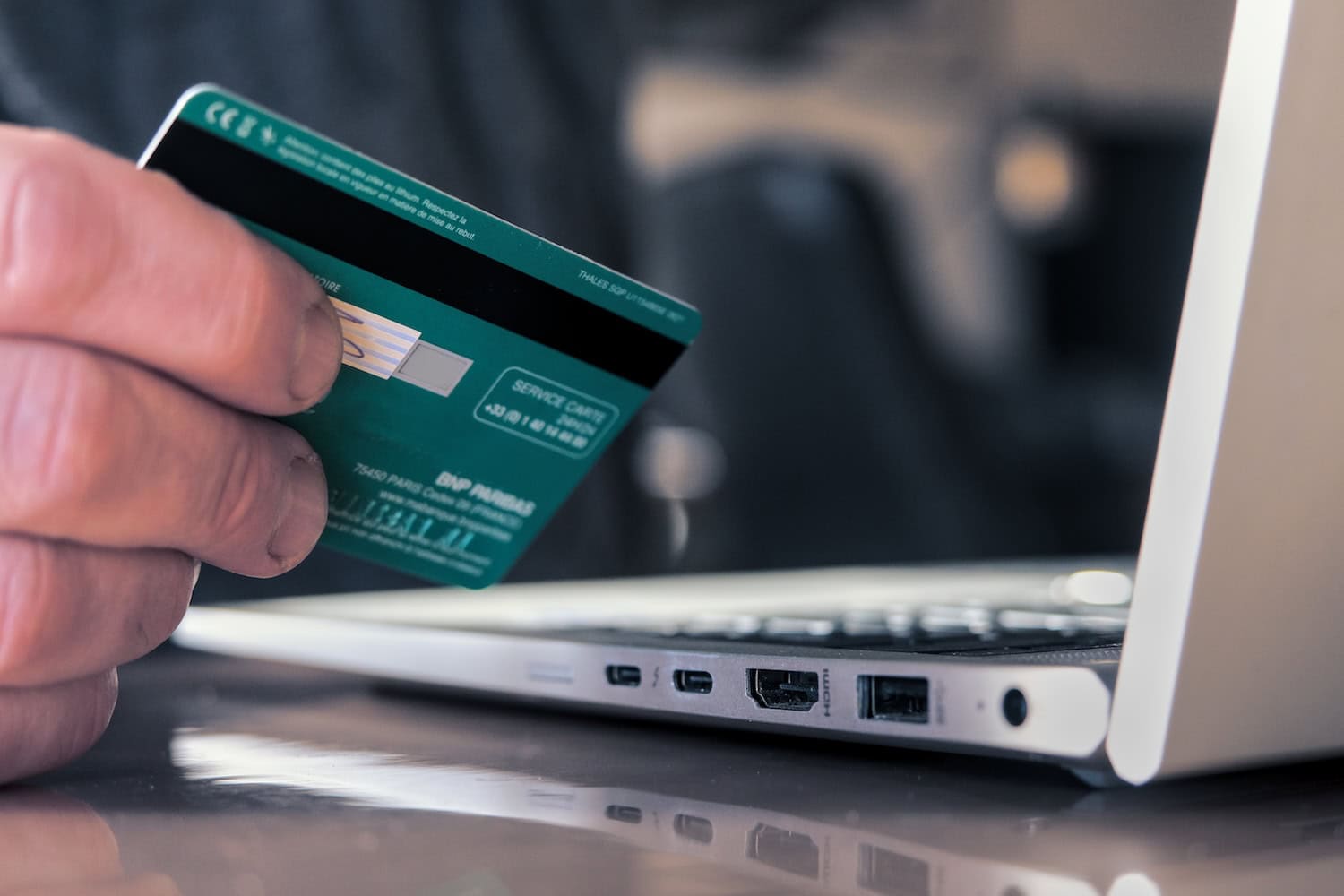 Mensch hält Bankkarte und sitzt am Laptop