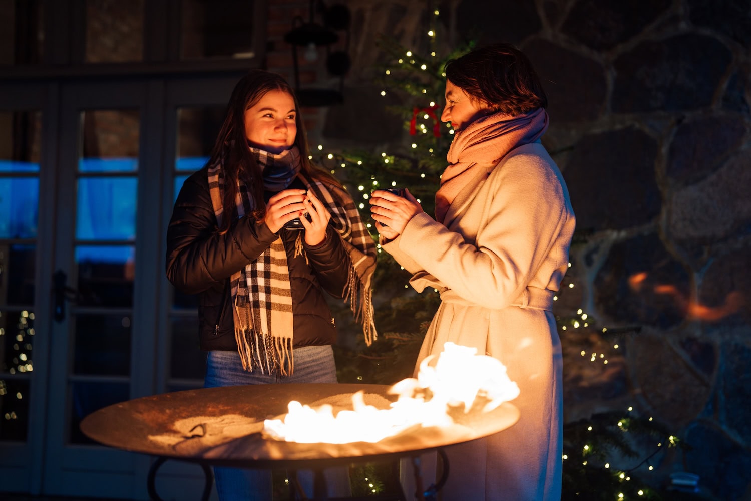 Mutter und Tochtr stehen an der Feuerstelle und trinken einen Glühwein
