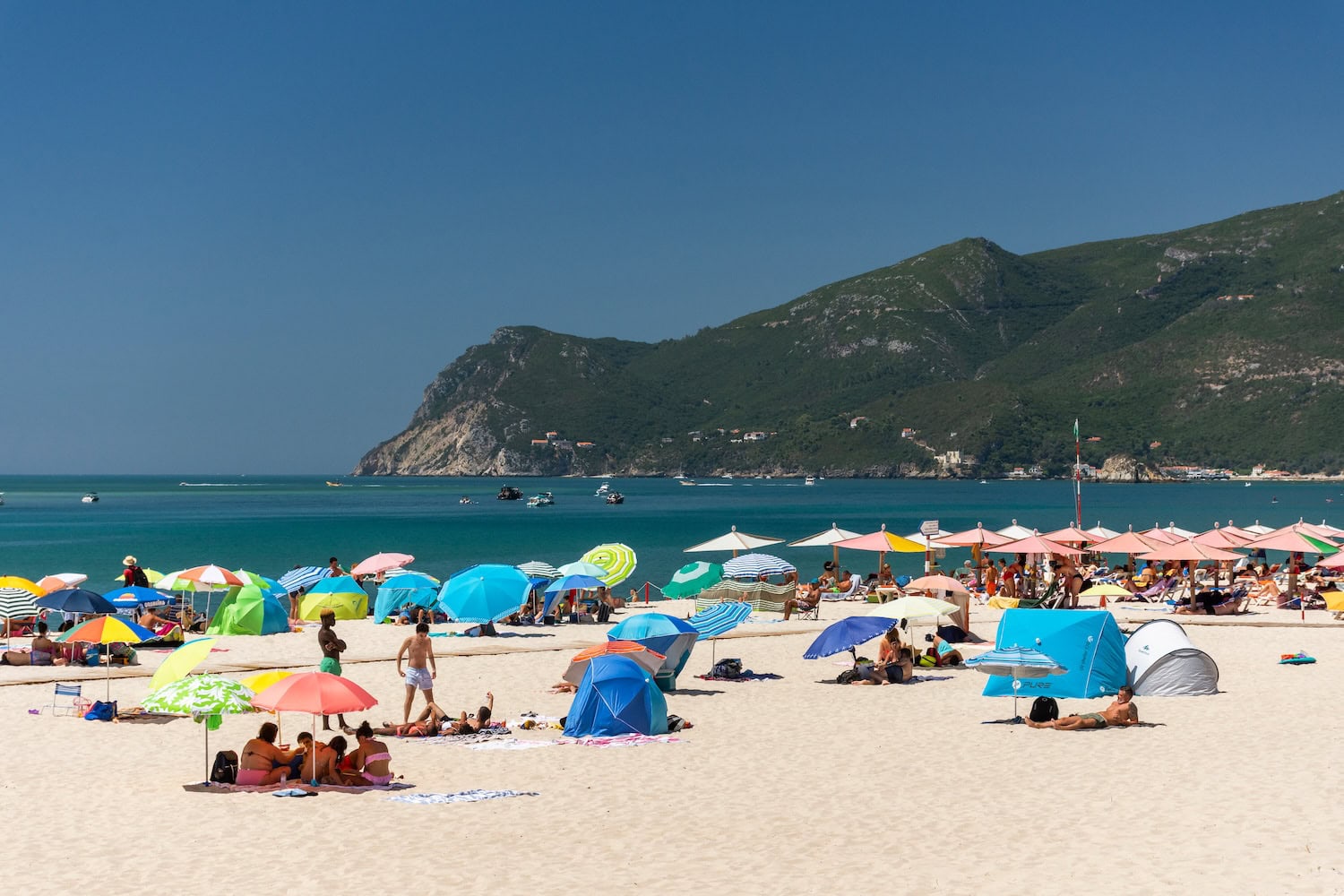 Menschen am Strand von Figueirinha mit Bergen im Hintergrund