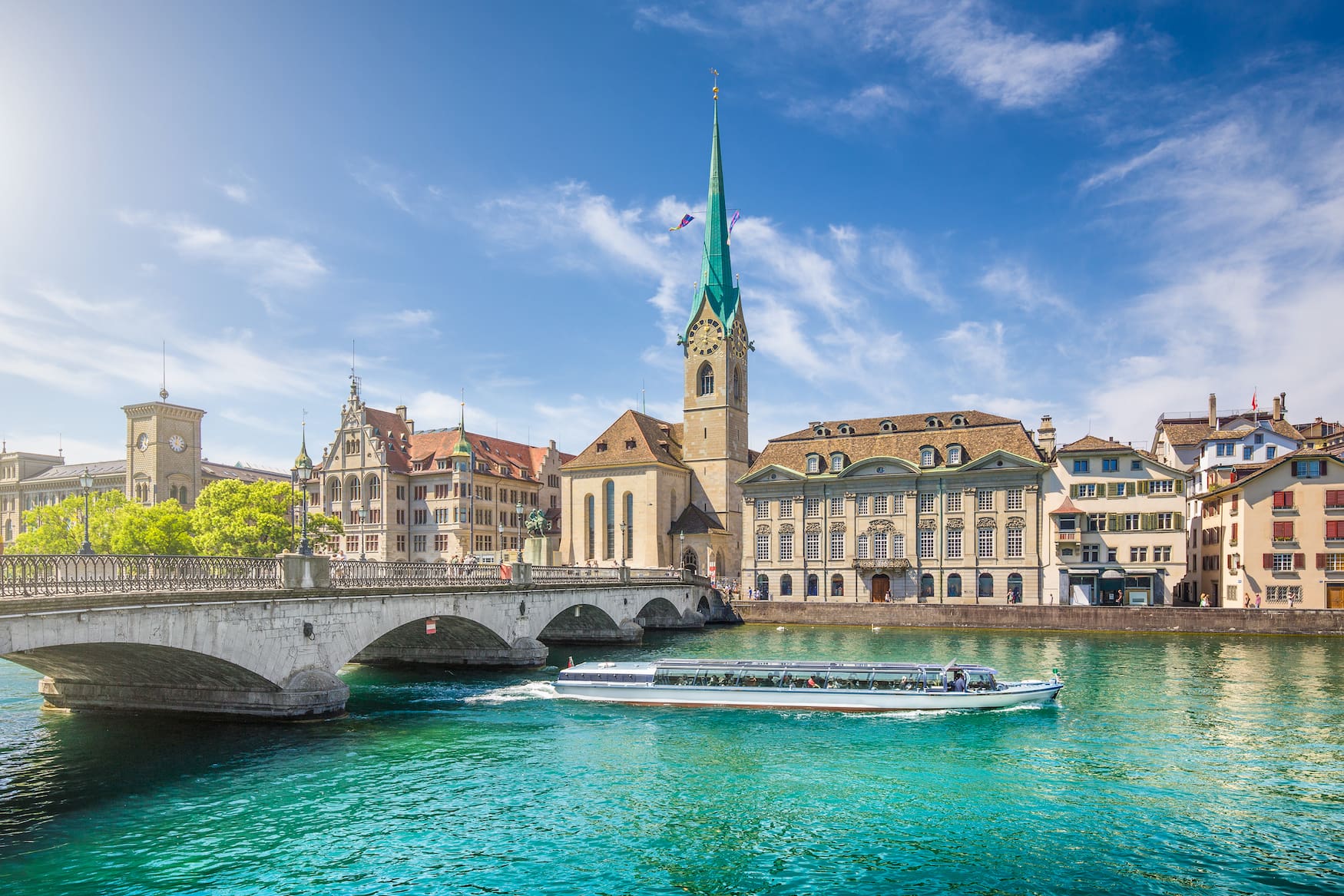 Schöne Aussicht auf das historische Stadtzentrum von Zürich mit der berühmten Fraumünsterkirche und Ausflugsboot auf der Limmat an einem sonnigen Tag mit blauem Himmel