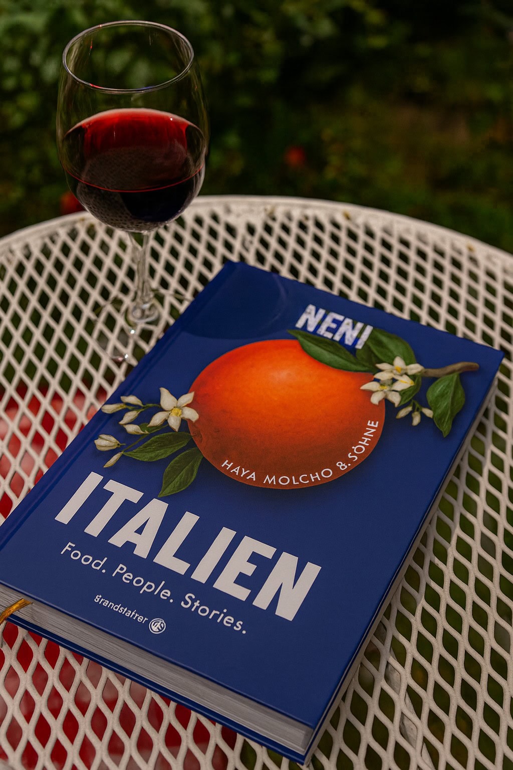 Das Buch Neni Italien auf einem Gartentisch mit einem Glas Rotwein. Eins der besten italienischen Kochbücher 2025.