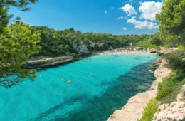 Eine paradiesische Bucht auf Mallorca mit türkisblauem Wasser, umgeben von hellem Sandstrand und dichtem, grünem Wald.