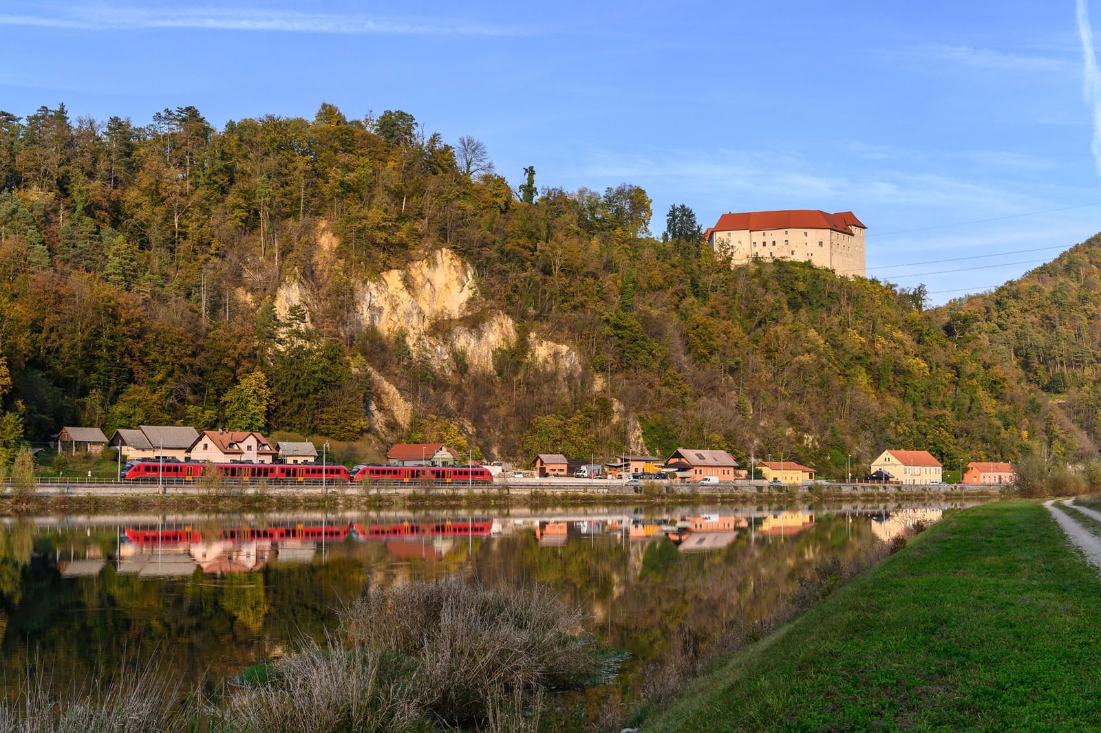 Ein Zug fährt in Slowenien an einer hügeligen Landschaft vorbei.
