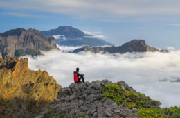 Wanderer, sitzend auf einem Berggipfel, der auf das Wolkenmeer schaut